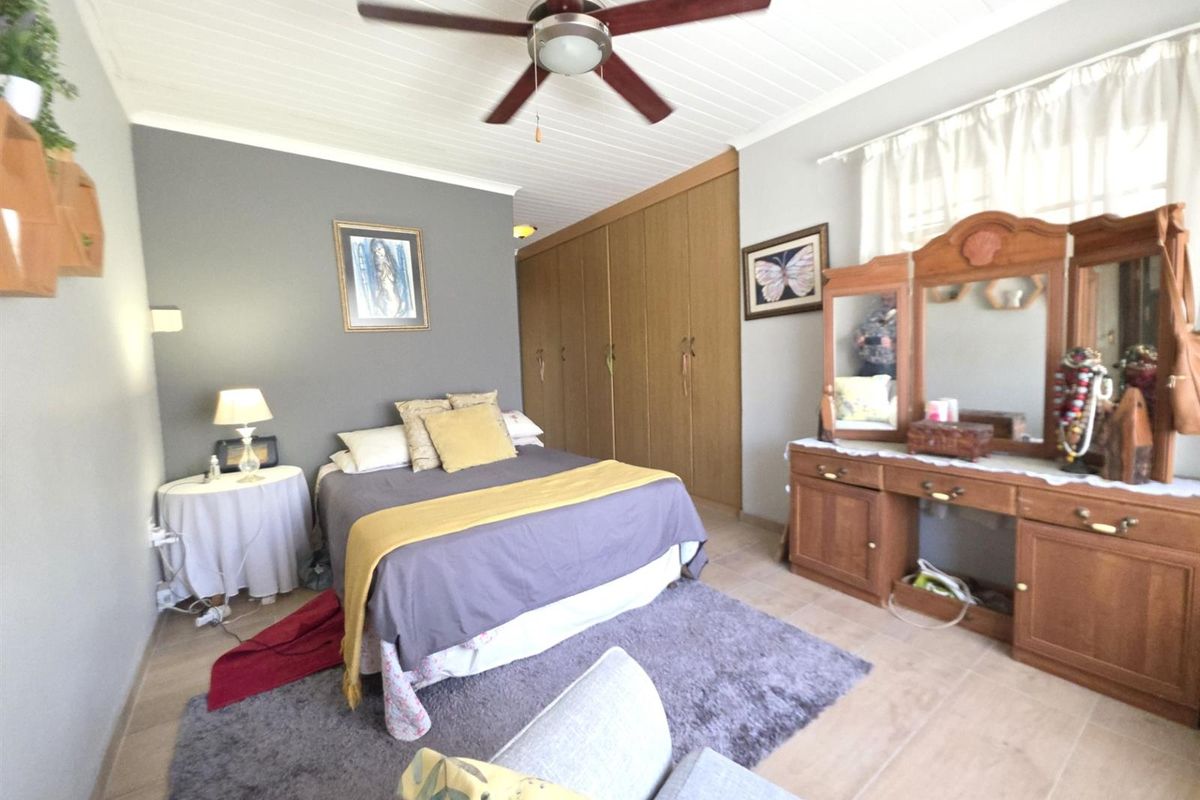 Spacious bedroom featuring built-in cupboards, a ceiling fan, and tiled flooring with a classic tongue and groove ceiling finish.