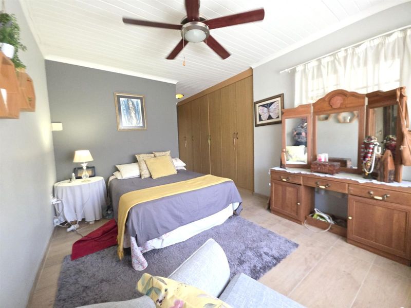 Spacious bedroom featuring built-in cupboards, a ceiling fan, and tiled flooring with a classic tongue and groove ceiling finish.