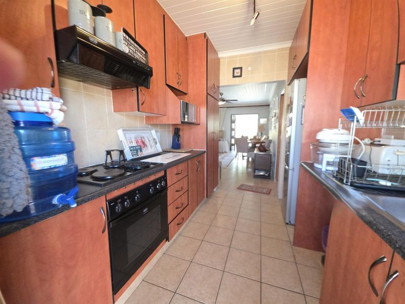 A functional galley-style kitchen featuring wood-finish cabinetry, built-in oven and hob, tiled flooring, and a tiled backsplash, leading through to the dining area.