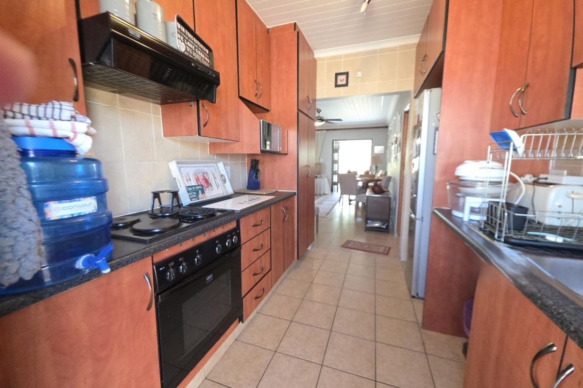 A functional galley-style kitchen featuring wood-finish cabinetry, built-in oven and hob, tiled flooring, and a tiled backsplash, leading through to the dining area.