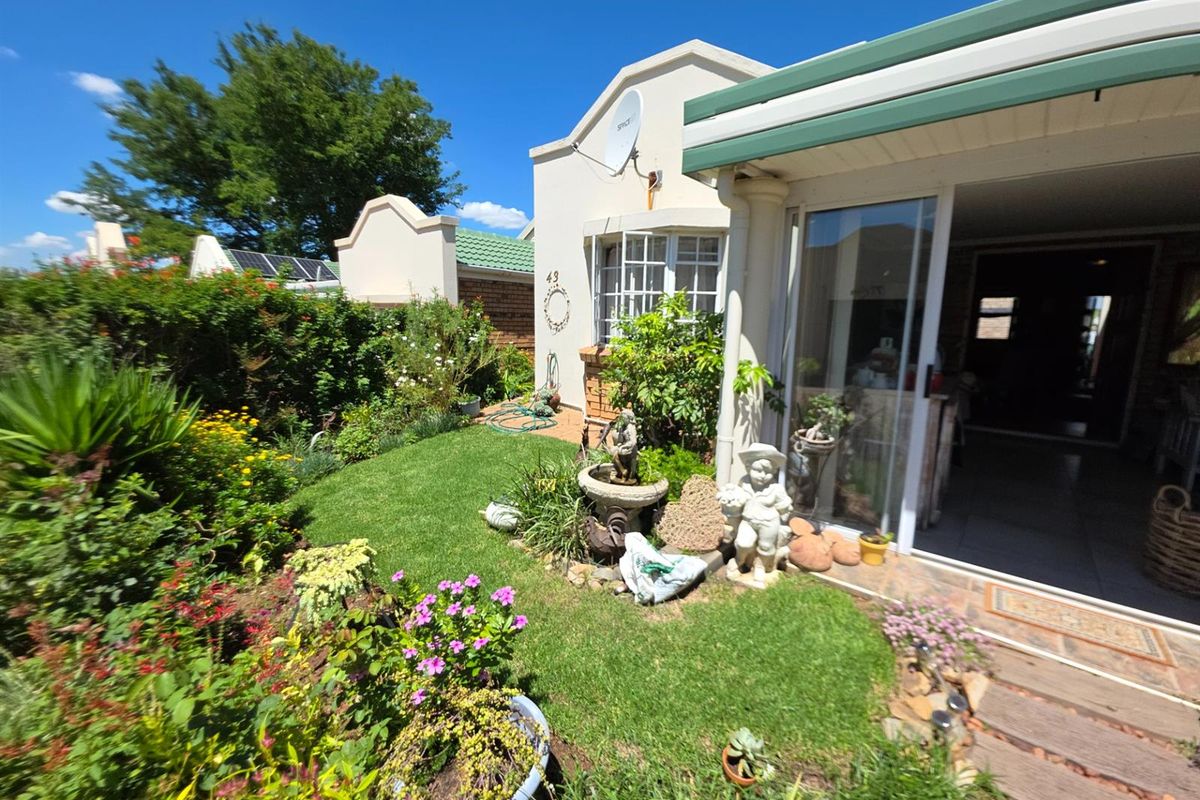 A well-maintained rear garden featuring a lush lawn, established flower beds, and a covered patio area with sliding glass door access to the home.