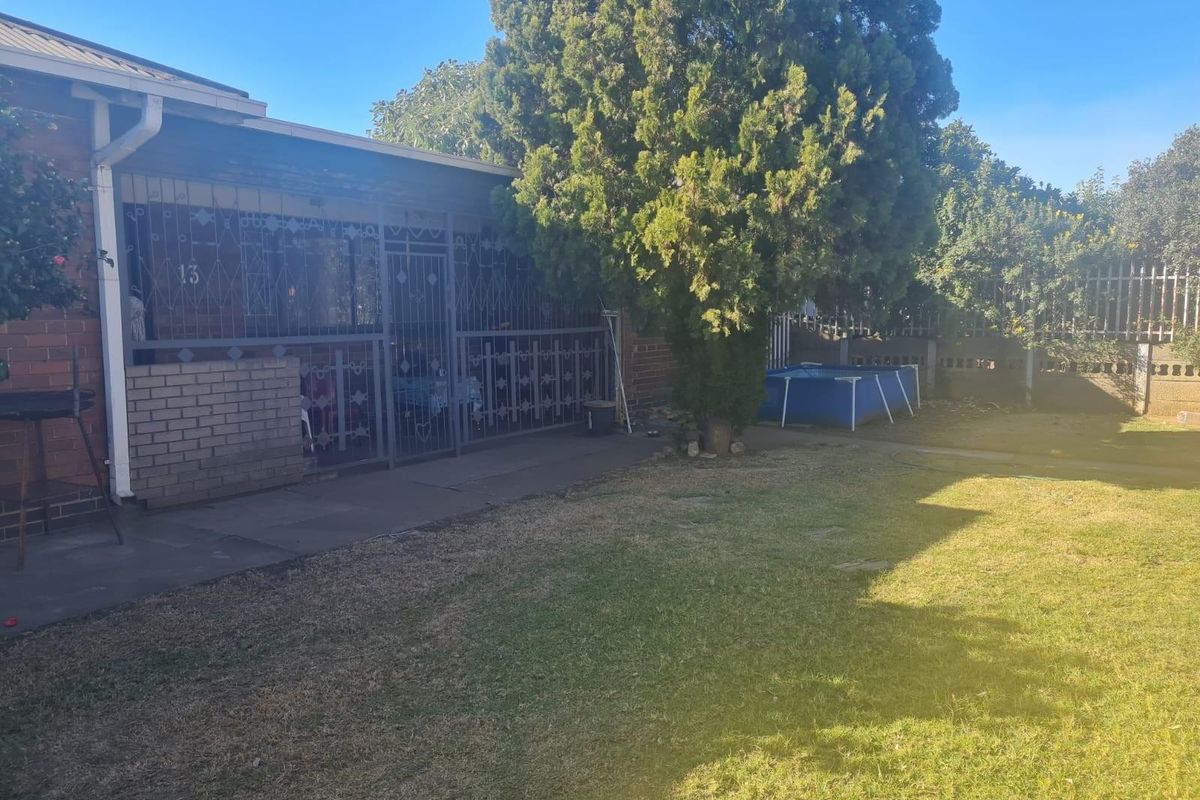 A rear view of the property featuring a covered patio area with security gates, a lawn, and perimeter fencing.