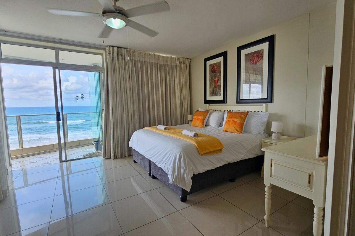Spacious bedroom featuring large sliding glass doors leading to a private balcony with direct ocean views and polished floor tiles.