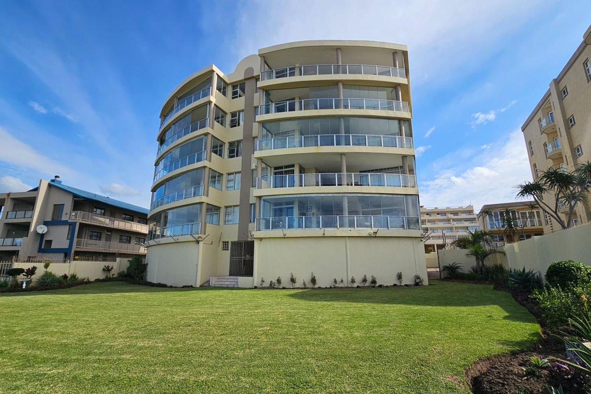 A view of the rear elevation of a multi-story apartment building featuring glass-enclosed balconies and a well-maintained lawn area.