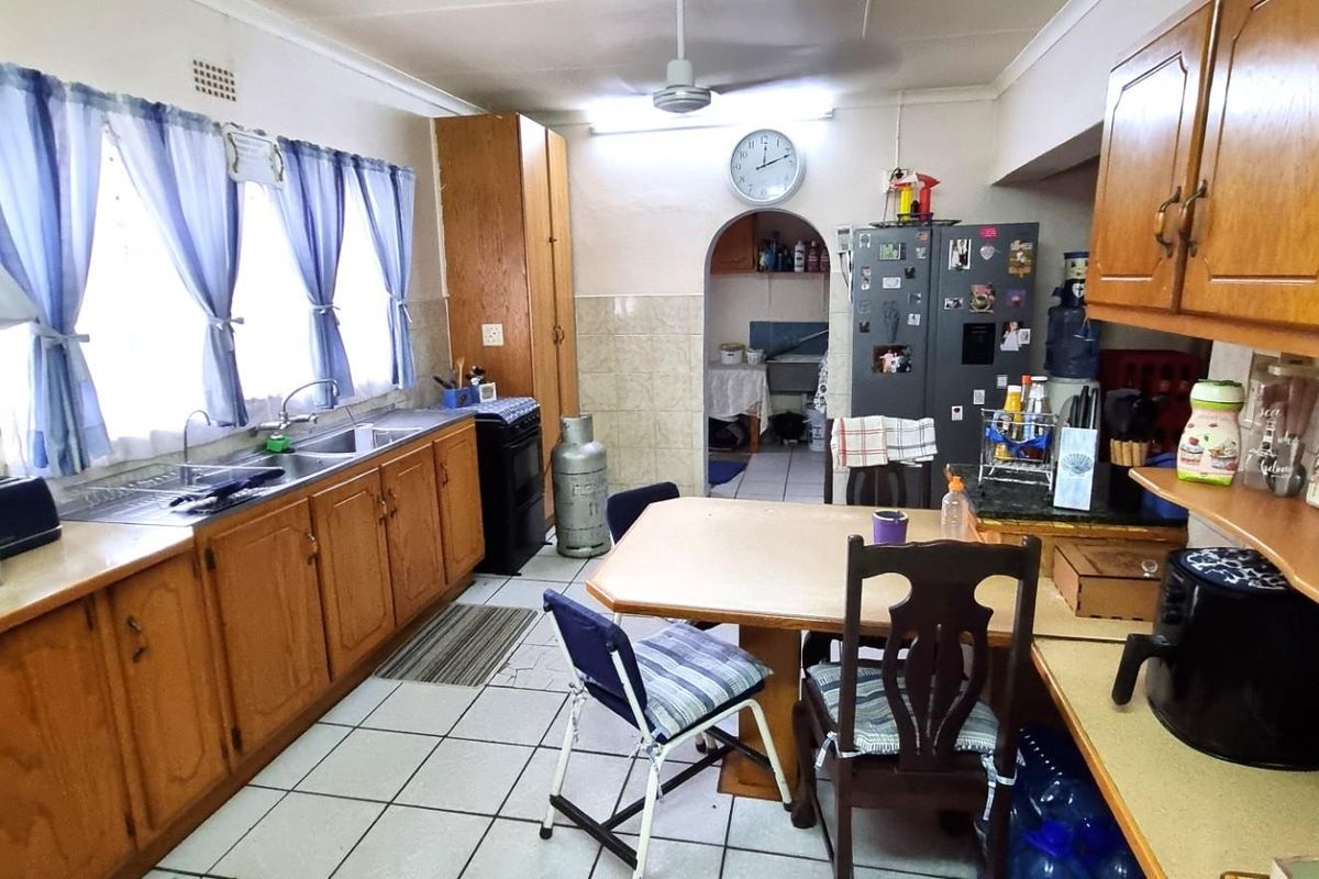 A functional kitchen featuring traditional wooden cabinetry, laminate countertops, a double sink, and tiled flooring, with an adjacent scullery area visible through an archway.
