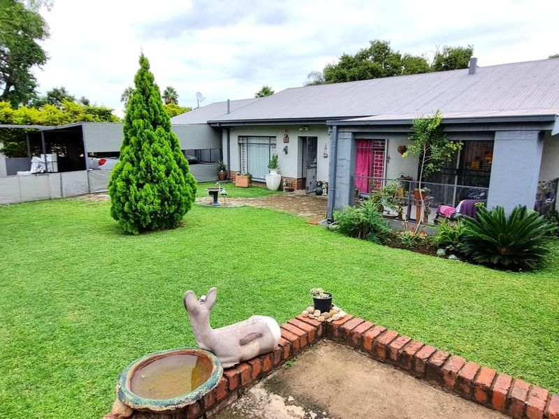A well-maintained rear garden featuring a lawn, established landscaping, and a covered patio area attached to the main house structure.