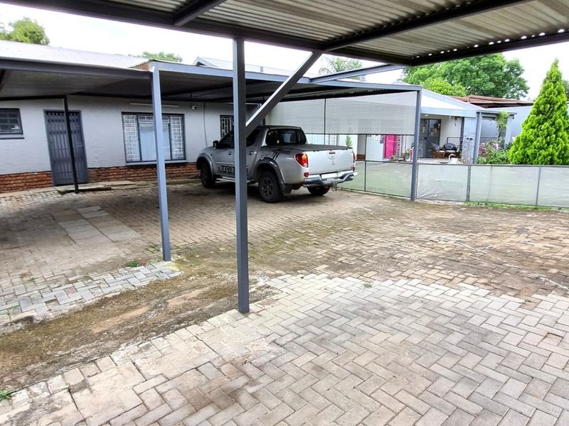 Rear exterior view featuring a large covered carport area with extensive paved driveway space and secure access points to the main dwelling.