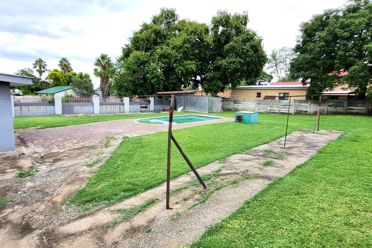 Spacious rear garden featuring a swimming pool, paved patio area, and perimeter walling, offering potential for landscaping and outdoor entertainment upgrades.