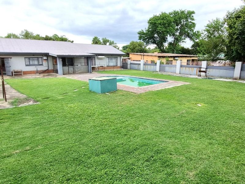 Spacious rear garden featuring a swimming pool, concrete pathways, perimeter walling, and a detached metal storage shed.