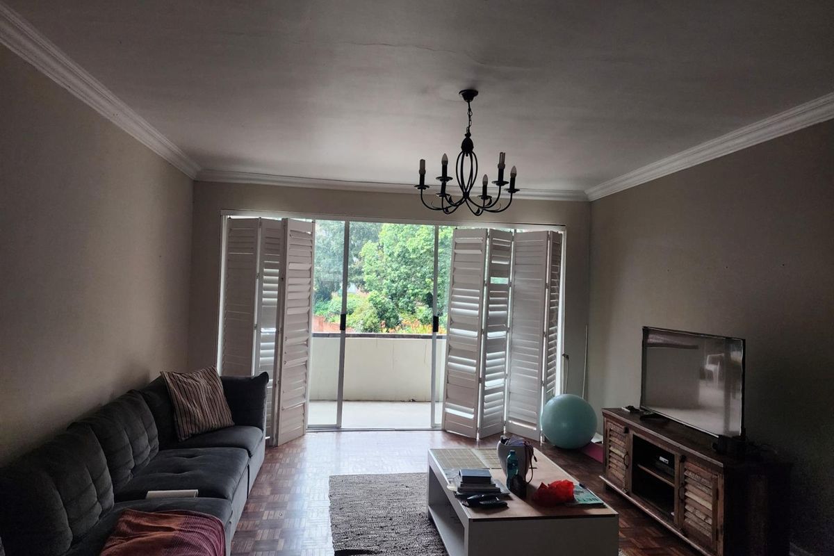 Spacious living room featuring parquet flooring, crown molding, and white plantation shutters opening onto a private balcony.
