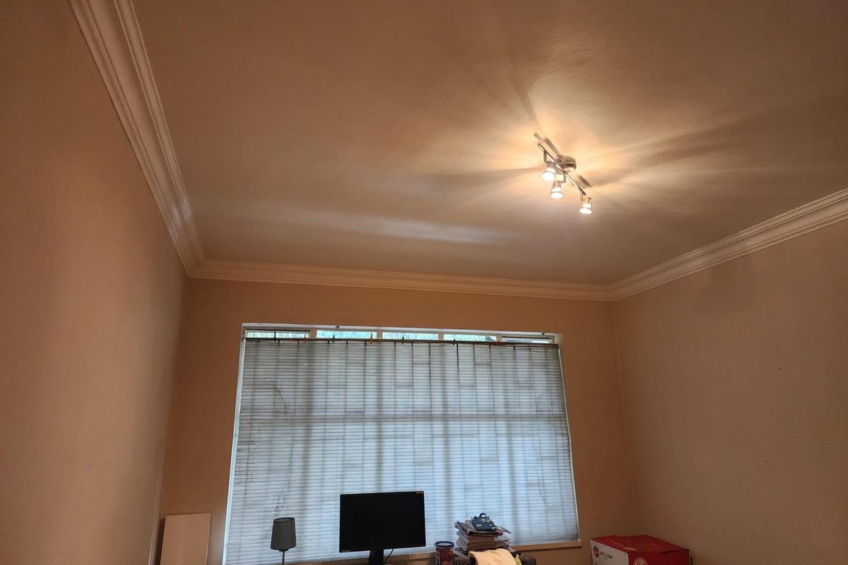 A bedroom featuring decorative ceiling cornicing and a large window with fitted blinds, providing natural light to the space.