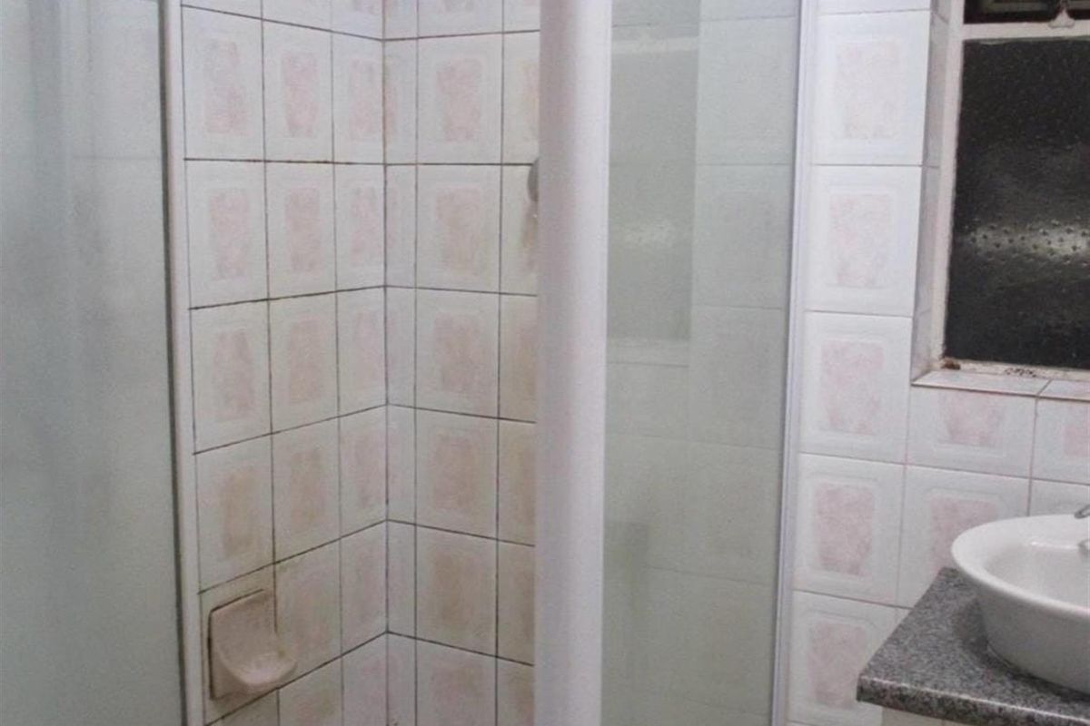 A functional bathroom featuring a shower enclosure with tiled walls and a vanity basin with a stone countertop.