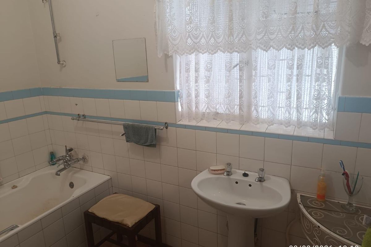A dated bathroom featuring a pedestal basin, built-in bathtub with shower mixer, and tiled walls, offering potential for a modern renovation.