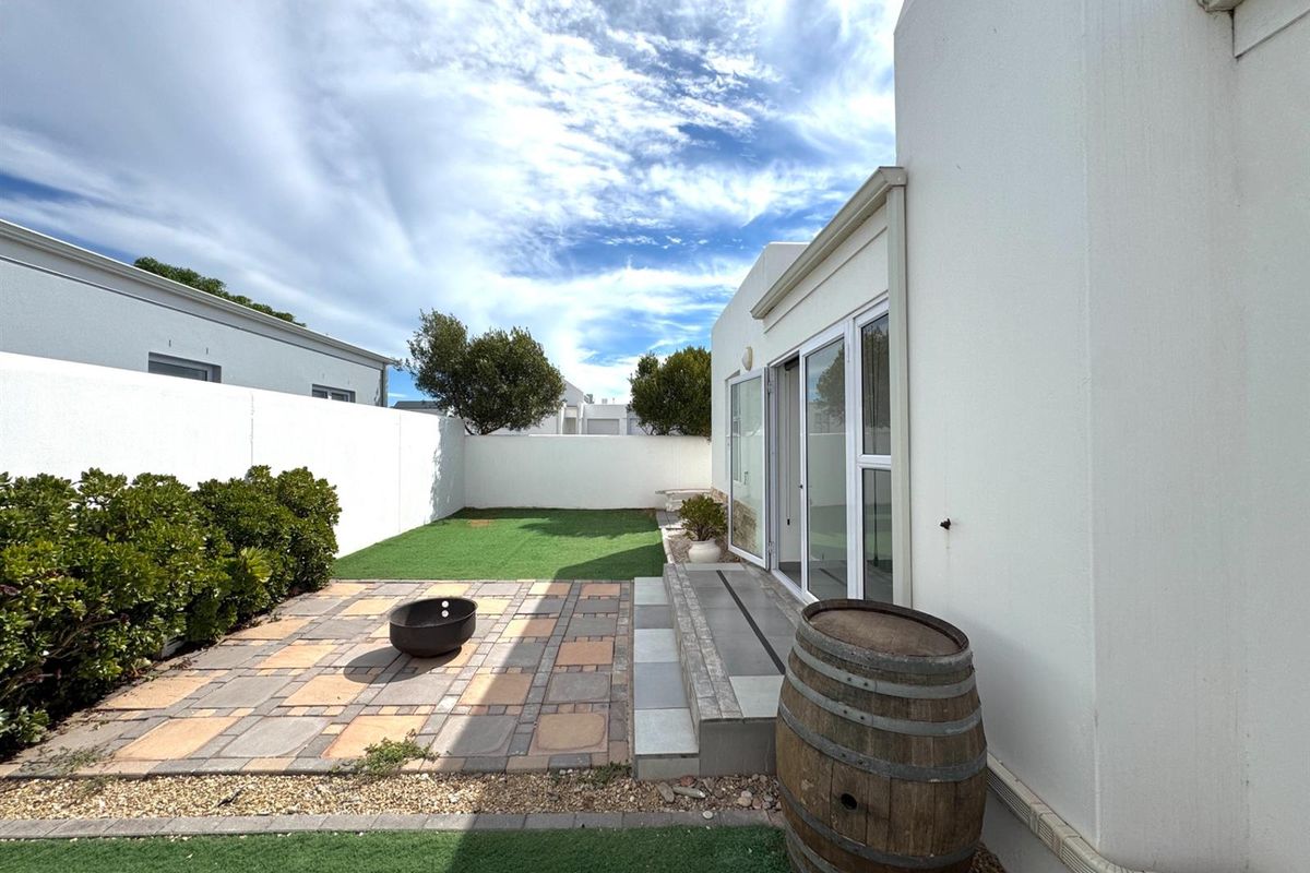 A private rear garden featuring a paved patio area, artificial lawn, and sliding glass doors providing seamless indoor-outdoor flow.