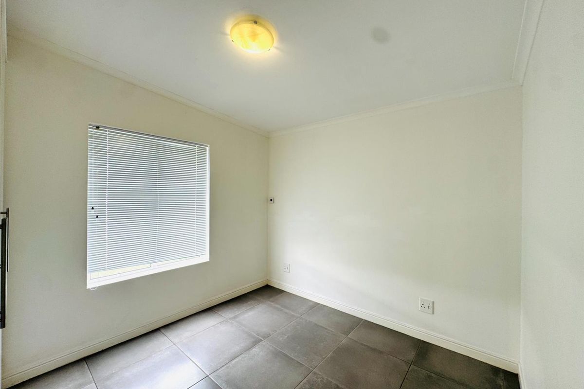 A clean, empty bedroom featuring neutral wall paint, dark floor tiles, and a window fitted with horizontal blinds.