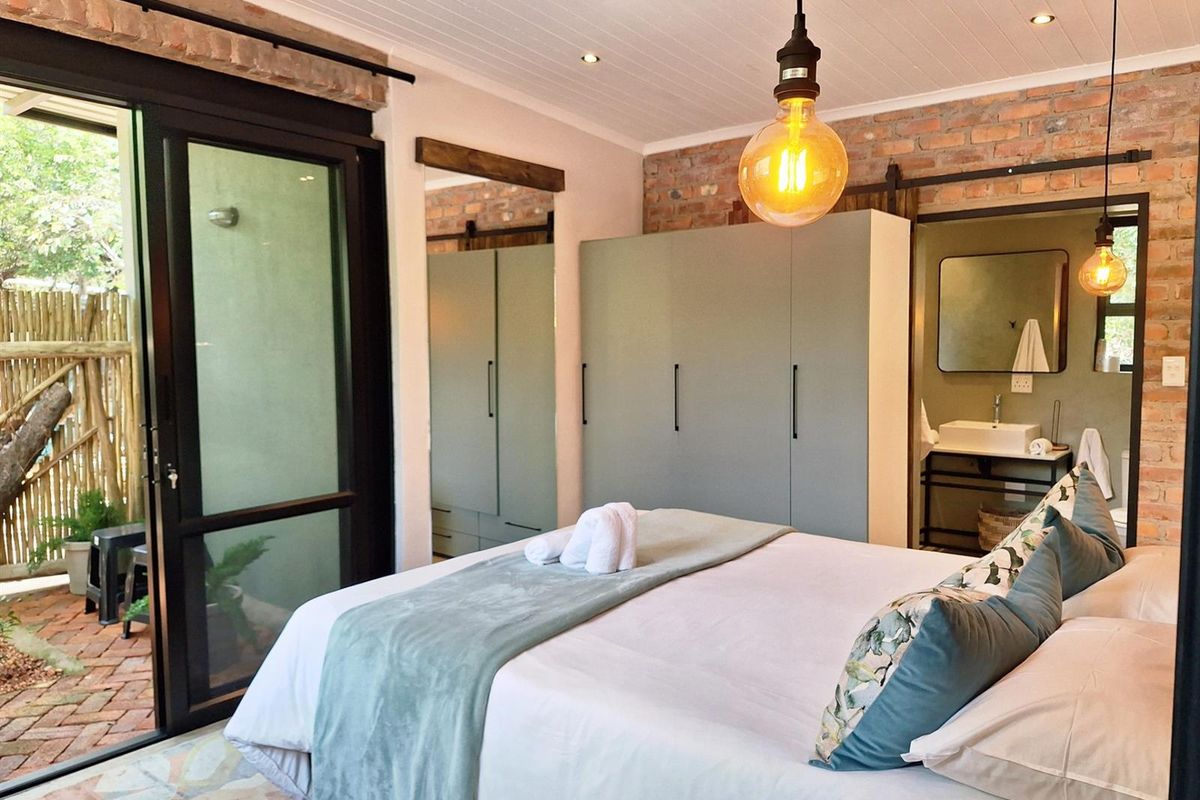 A well-appointed bedroom featuring exposed brick walls, built-in cabinetry, and sliding glass doors providing direct access to a private outdoor patio area.
