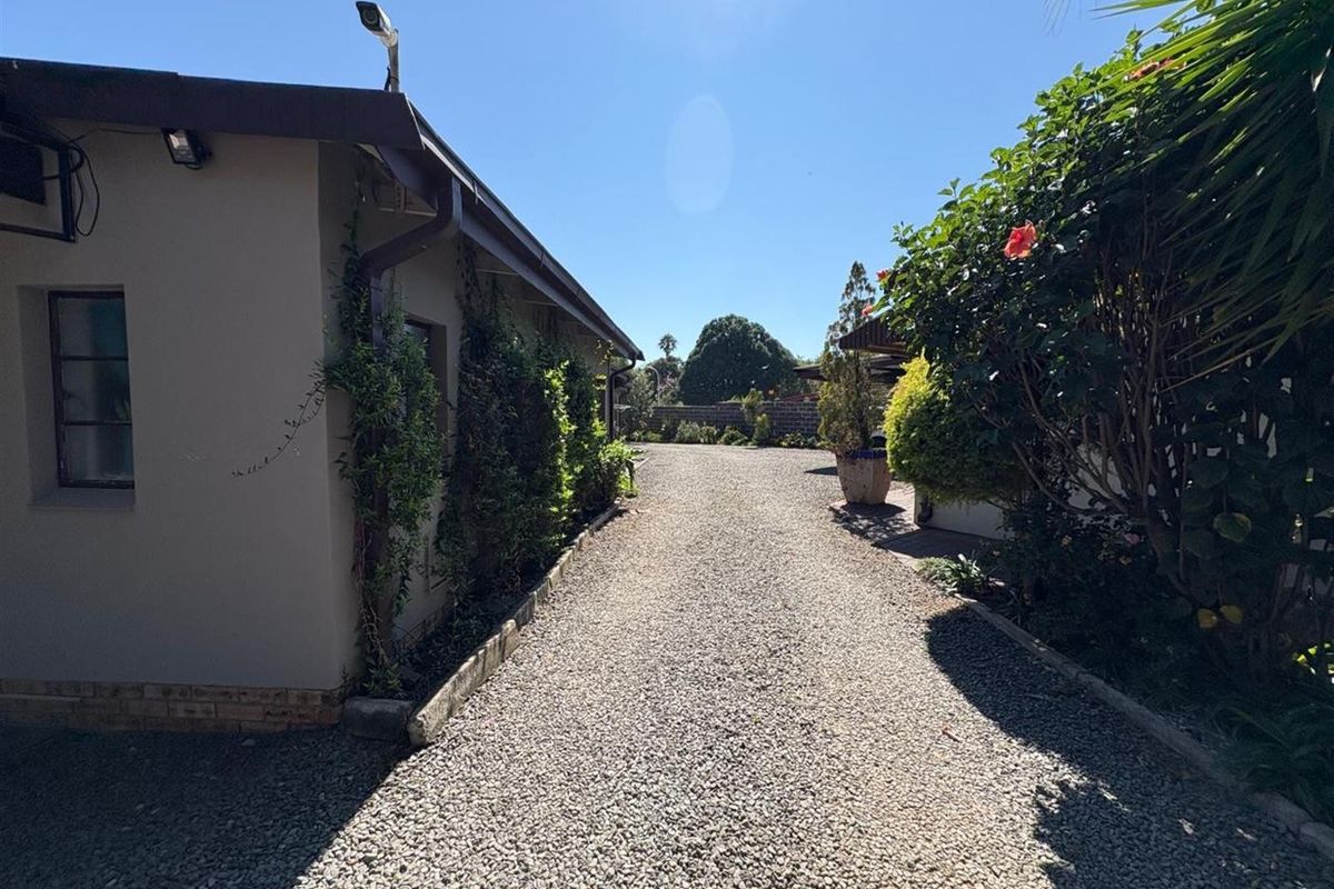 A gravel driveway leading along the side of the house, featuring established garden landscaping and exterior security lighting.