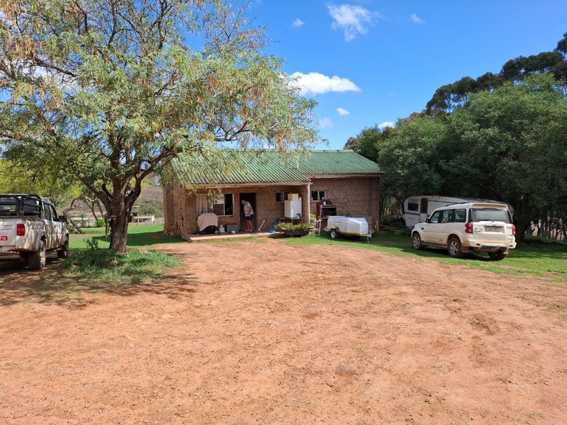 A rustic farm-style dwelling featuring a covered front porch, corrugated metal roof, and natural brick exterior, set within a spacious rural landscape.