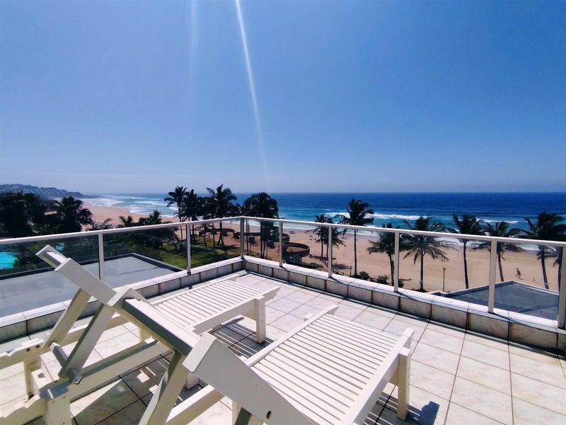 Spacious balcony featuring tiled flooring and a modern glass balustrade, offering panoramic ocean and beach views.