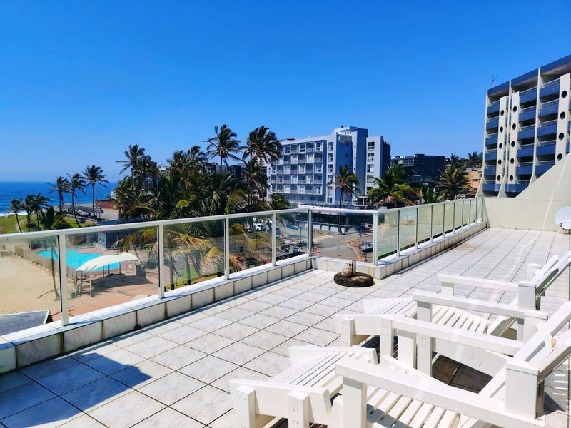 Spacious balcony featuring tiled flooring and a modern glass balustrade, offering expansive coastal and urban views.
