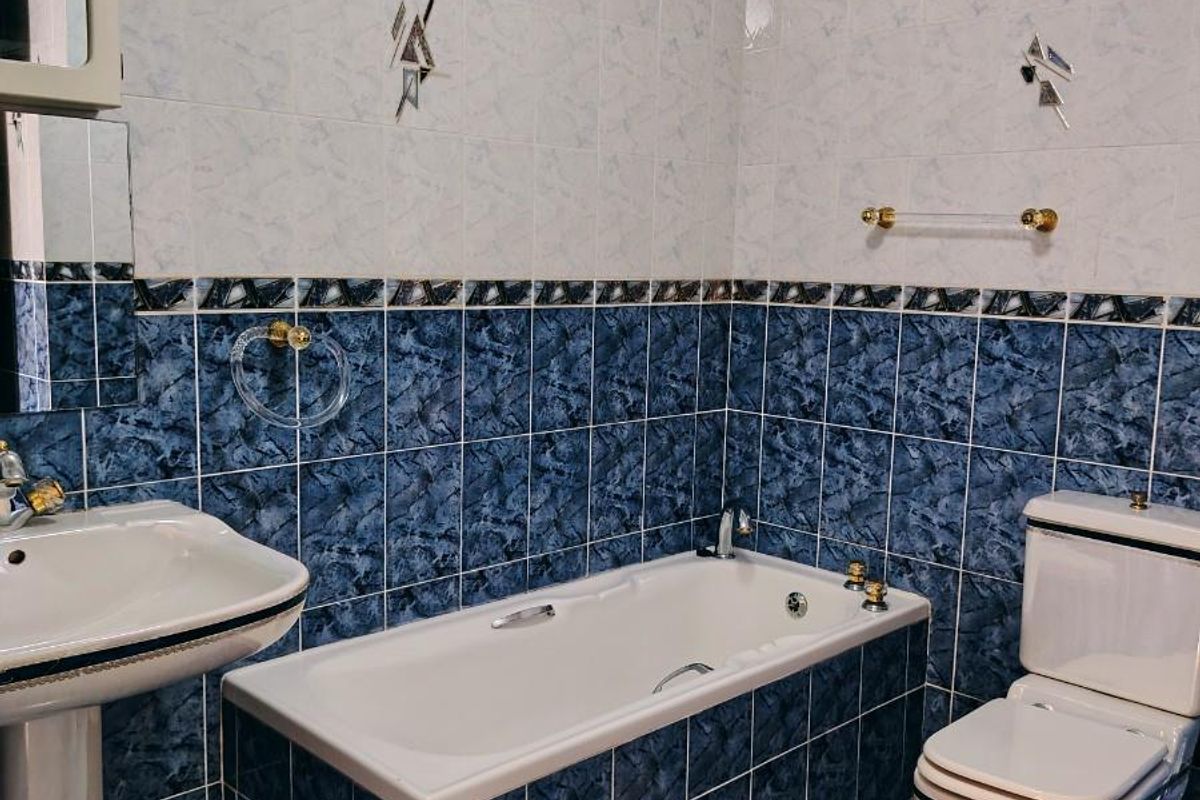 A functional bathroom featuring a pedestal sink, a built-in bathtub, and a toilet, finished with blue and white patterned wall and floor tiles.