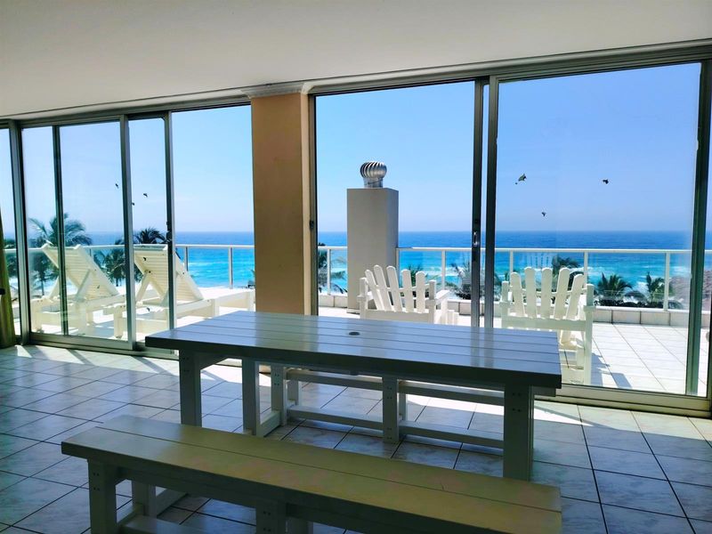 Spacious enclosed balcony featuring large sliding glass doors, tiled flooring, and panoramic ocean views, providing a seamless transition to the outdoor terrace.