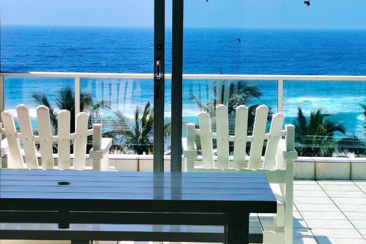 A bright living area featuring large sliding glass doors that open onto a balcony with stunning ocean views and a glass balustrade.