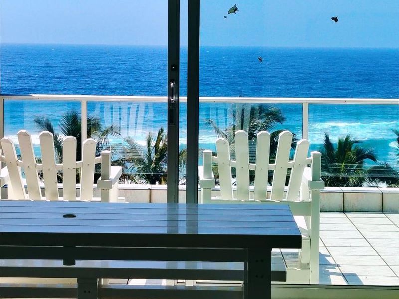 A bright living area featuring large sliding glass doors that open onto a balcony with stunning ocean views and a glass balustrade.