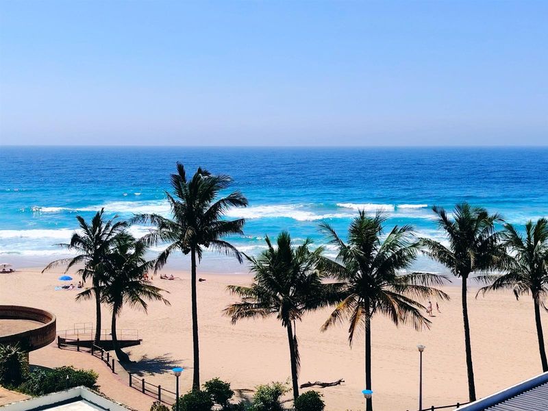 A scenic elevated view overlooking a sandy beach, ocean waves, and palm trees, showcasing the property's prime coastal location.