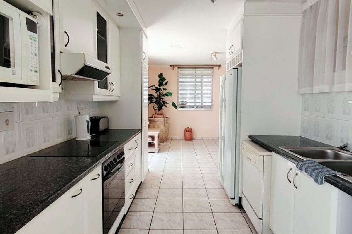 A functional galley-style kitchen featuring white cabinetry, dark granite countertops, integrated oven, hob, and extractor fan with tiled flooring throughout.