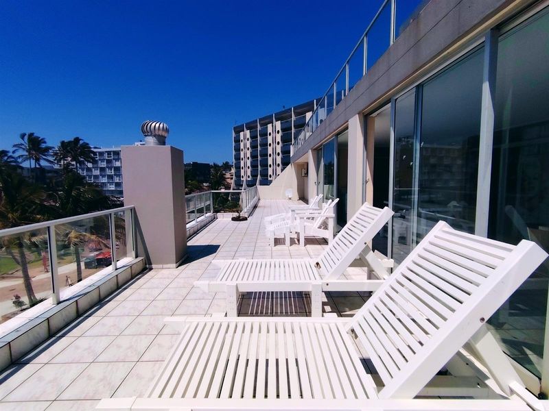 Spacious apartment balcony featuring tiled flooring, glass balustrades, and large sliding door access to the interior living space.