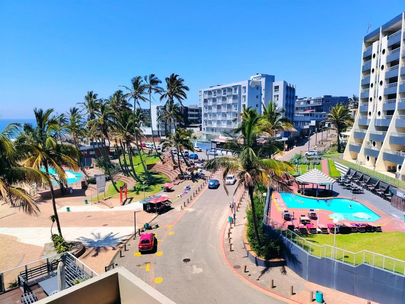 Elevated view overlooking the coastal street, swimming pool area, and surrounding apartment buildings in a vibrant beachside neighborhood.