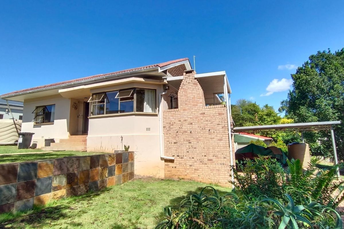 A rear view of the house featuring a brick chimney, covered patio area, and a landscaped garden with a stone-clad retaining wall.