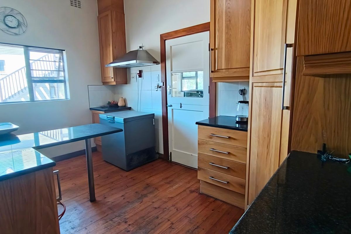 A functional kitchen featuring timber cabinetry, dark stone countertops, a stainless steel extractor fan, and timber flooring with a stable door entrance.