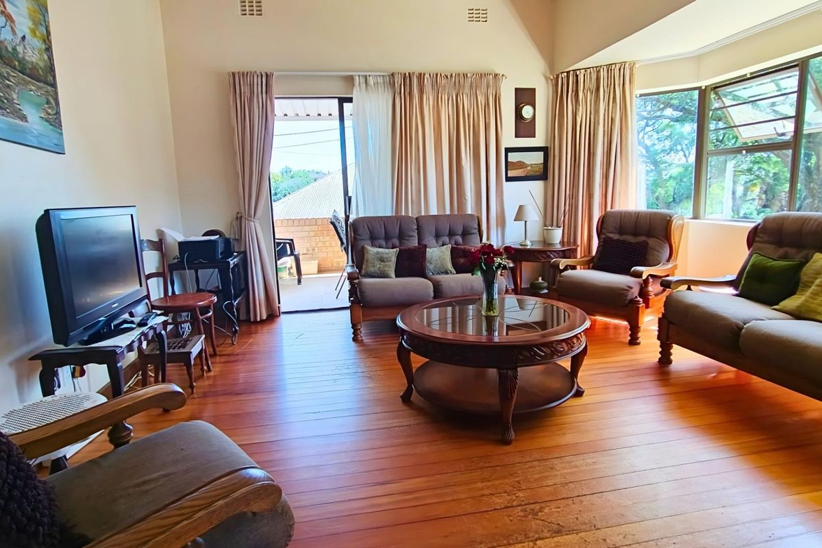 A spacious living room featuring polished timber flooring, high vaulted ceilings, and large windows that provide natural light and access to an outdoor patio area.