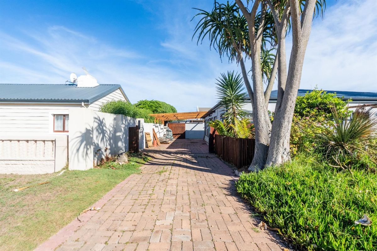 A paved driveway leading to a rear area featuring a timber pergola, boundary walls, and established garden landscaping.