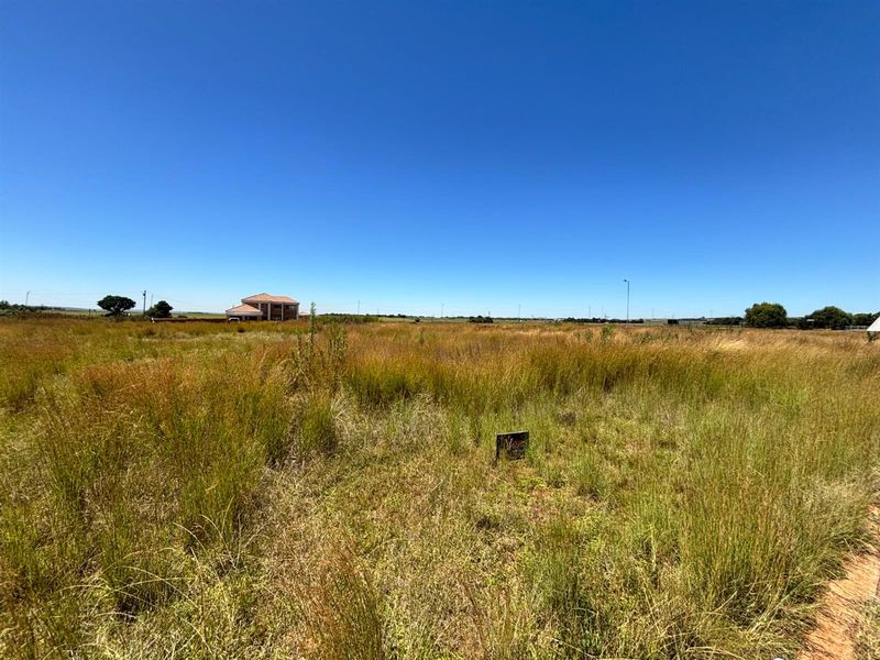 A wide-angle view of a vacant residential plot featuring natural grassland and surrounding neighborhood development.