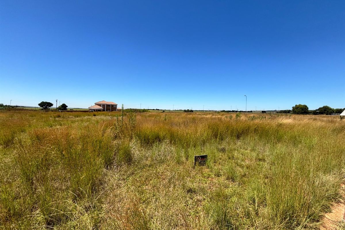 A wide-angle view of a vacant residential plot featuring natural grassland and surrounding neighborhood development.