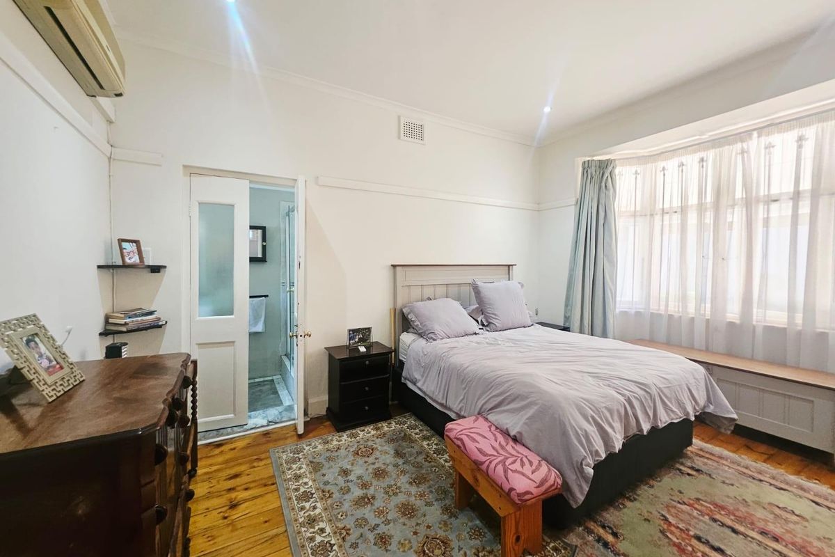 A bedroom featuring polished timber flooring, a bay window with built-in seating, and an en-suite bathroom access.
