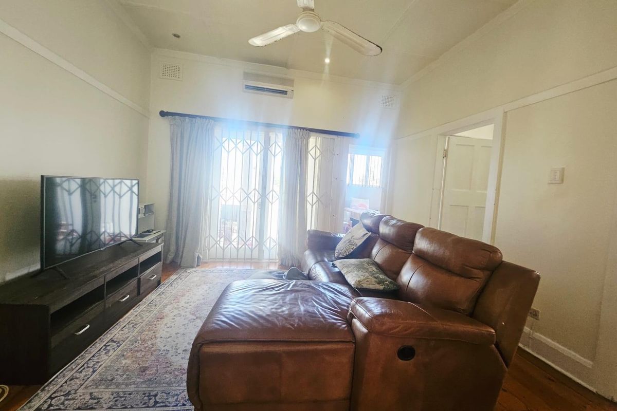 A comfortable living room featuring polished timber flooring, a ceiling fan, and a wall-mounted air conditioning unit, with access to an outdoor area.