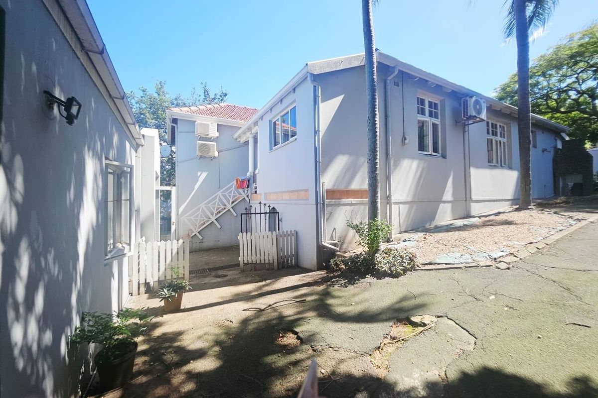 Exterior view of the property showing the rear facade, paved driveway area, and external air conditioning units.