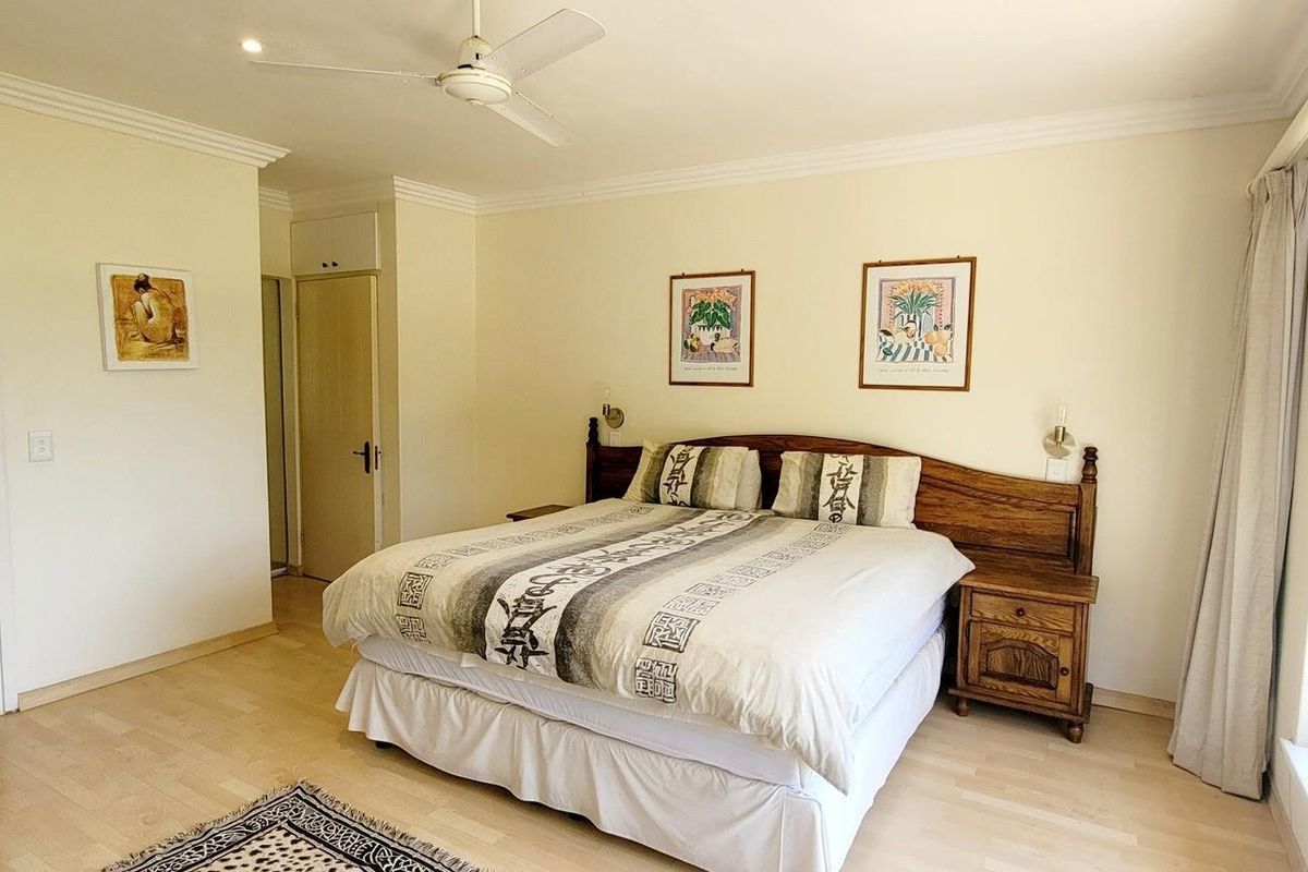 Spacious bedroom featuring light wood-look flooring, a ceiling fan, and an en-suite bathroom entrance, with large windows providing natural light.