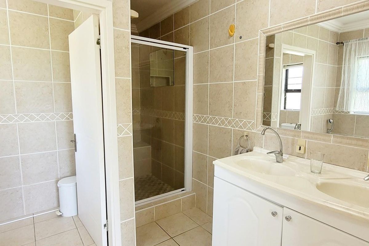 A functional bathroom featuring a double vanity with integrated sinks, a glass-enclosed shower, and full-height wall tiling.