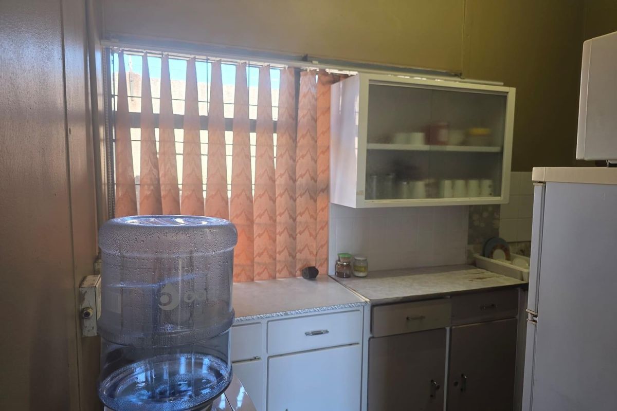 A compact kitchen area featuring dated cabinetry, laminate countertops, and a window with vertical blinds.