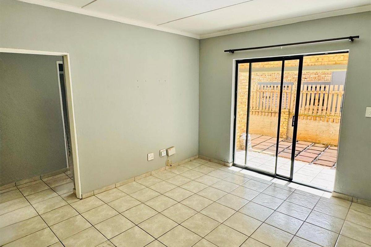 An empty living room featuring ceramic floor tiles and a sliding glass door providing direct access to the rear patio area.