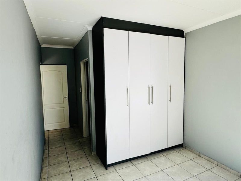 A clean, empty bedroom featuring neutral grey walls, tiled flooring, and a modern built-in wardrobe with white doors and dark framing.