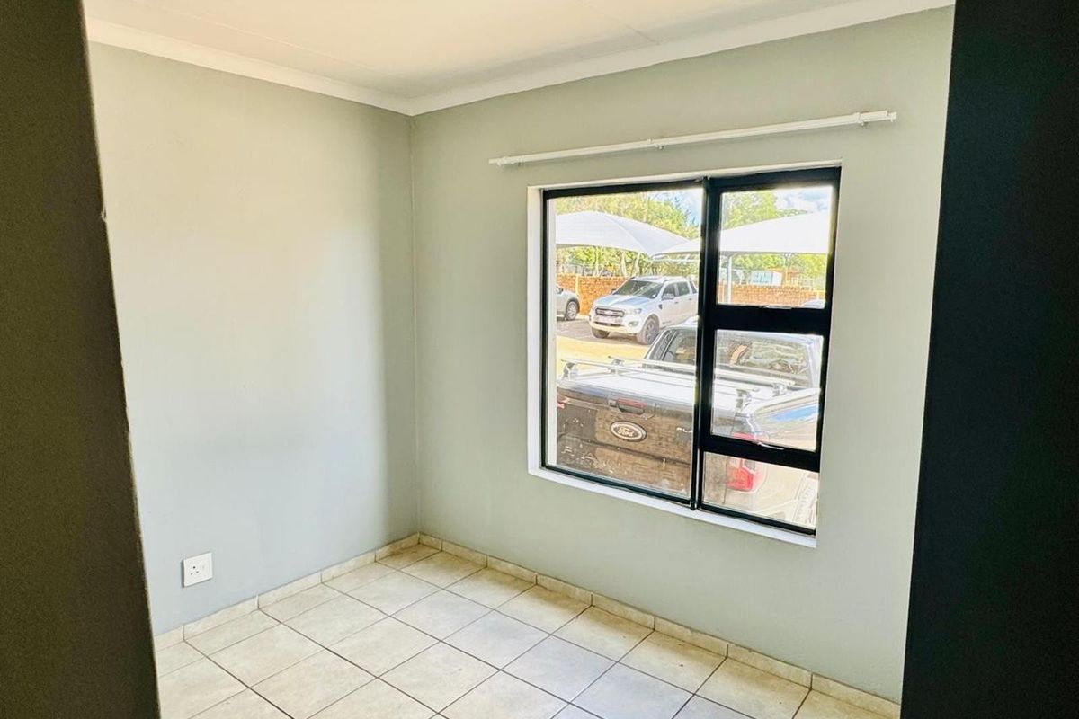 A clean, empty bedroom featuring neutral wall paint, tiled flooring, and a large aluminium-framed window with an integrated curtain rail.