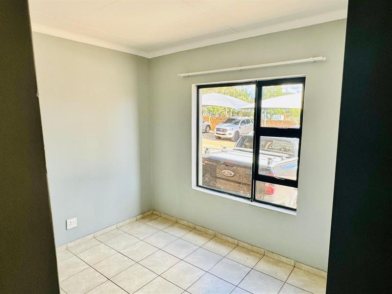 A clean, empty bedroom featuring neutral wall paint, tiled flooring, and a large aluminium-framed window with an integrated curtain rail.