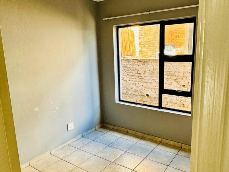 An empty bedroom featuring neutral tiled flooring, grey walls, and an aluminium-framed window, providing a blank canvas for personalization.
