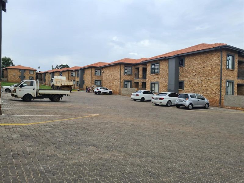 Exterior view of a multi-unit townhouse complex featuring face brick construction, tiled roofing, and a large paved parking area.